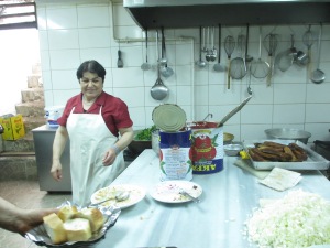 kitchen with utensils on wall, steel kitchen bench, woman in white apron, and pile of chopped onion