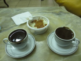 two cups and saucers filled with dark liquid. Plastic dish filled with cinnamon coated light liquid